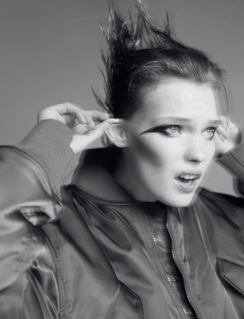Close-up black and white portrait of a young adult woman with her fingers in her ears, wearing a jacket, with dramatic eyeliner.
