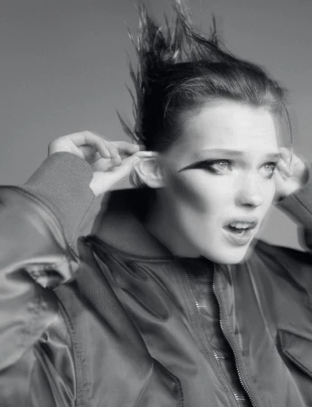 Close-up black and white portrait of a young adult woman with her fingers in her ears, wearing a jacket, with dramatic eyeliner.