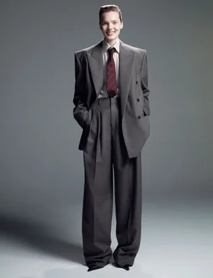 Model wearing an oversized grey double-breasted suit with a striped shirt and red tie against a grey backdrop.