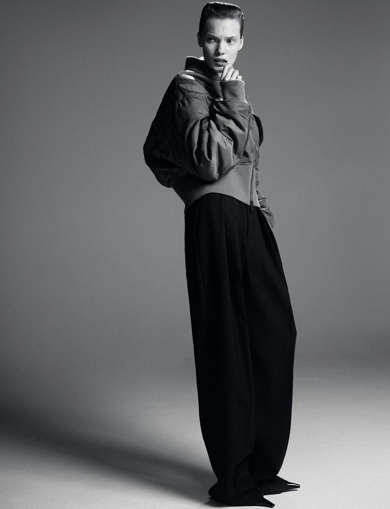 Model Penelope Ternes wearing a Saint Laurent bomber jacket and black trousers against a grey seamless studio background.