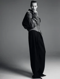 Model Penelope Ternes wearing a Saint Laurent bomber jacket and black trousers against a grey seamless studio background.
