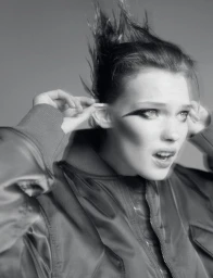 Monochrome portrait of a model with spiked hair wearing a bomber jacket against a grey background