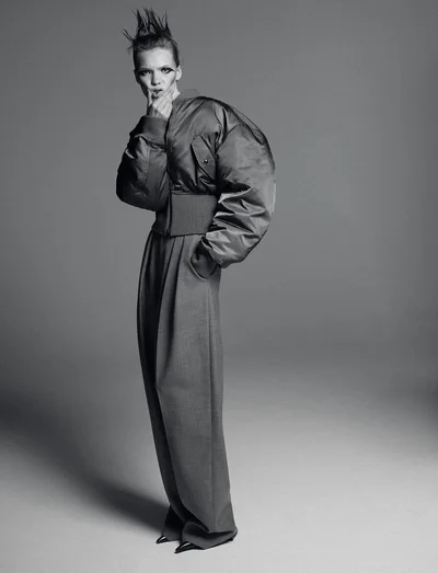 Model in voluminous bomber jacket and high-waisted trousers with spiked hair against a grey seamless background