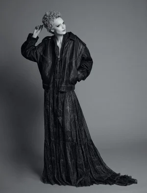 Model in black leather jacket and long patterned dress posing against a grey studio backdrop for Re-Edition Magazine.
