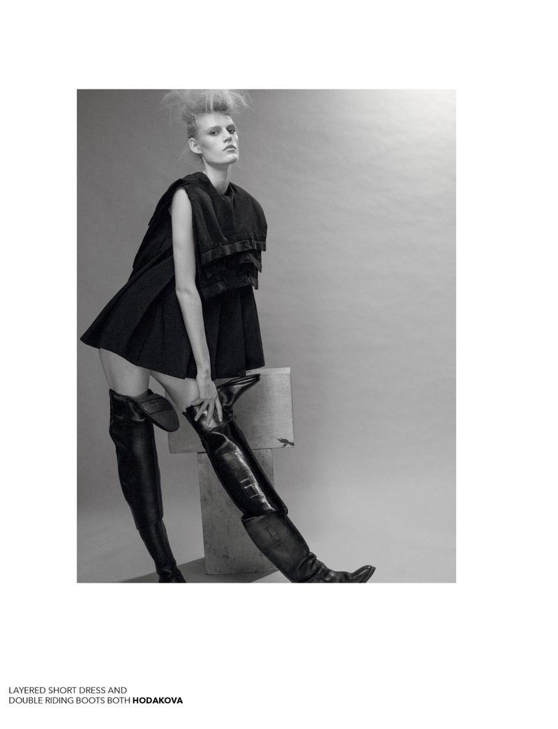 A fashion photo features a slender woman in a short black dress and thigh-high leather boots, posing against a neutral gray backdrop.