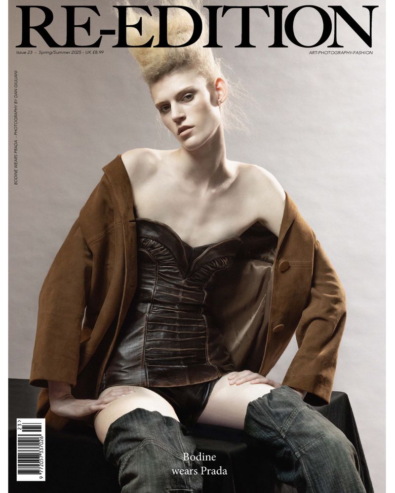 Magazine cover featuring a single fashion model with stylized blonde hair wearing a brown jacket and a black corset. The model is sitting.