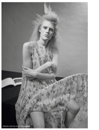 Model Bodine Van Galen in a patterned sleeveless dress seated against a grey backdrop with an open book nearby