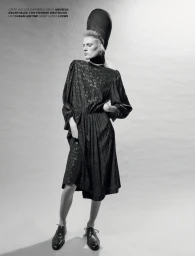 Model wearing a dark patterned dress and tall structured hat posing against a seamless light background for Re-Edition Magazine.