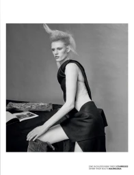 Model with structured blonde hair posing next to an open book on a draped table in a black and white editorial shoot