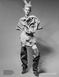 Monochrome fashion portrait of a model with spiky hair wearing a deconstructed layered shirt and tall slouchy boots.