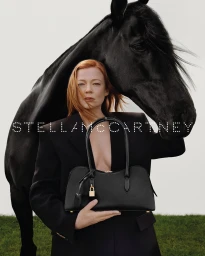 Sarah Snook wearing a black blazer holding a black handbag next to a black horse