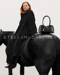 Sarah Snook sitting on a black horse wearing a black coat next to a black handbag for Stella McCartney