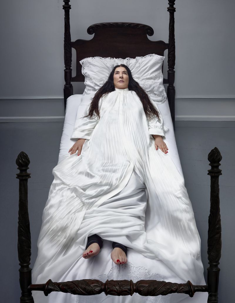 Overhead shot of a woman lying on a dark wood, four-poster bed, covered by a white, vintage-style bedspread and pillow in a simple bedroom.