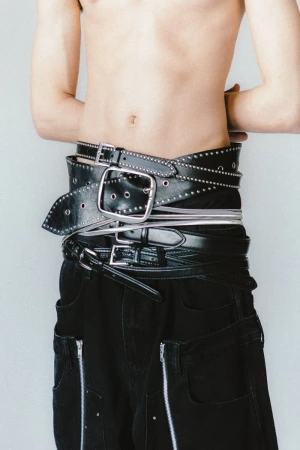 Torso shot of a person wearing black pants with zipper details and multiple black belts wrapped around their waist in a studio setting.