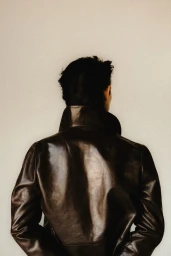 Model seen from behind wearing a dark leather jacket against a neutral studio background