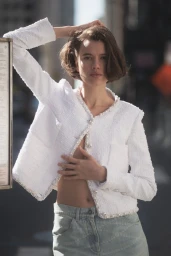 Model with short brown hair wearing a white textured tweed jacket and light denim jeans against an outdoor city street backdrop