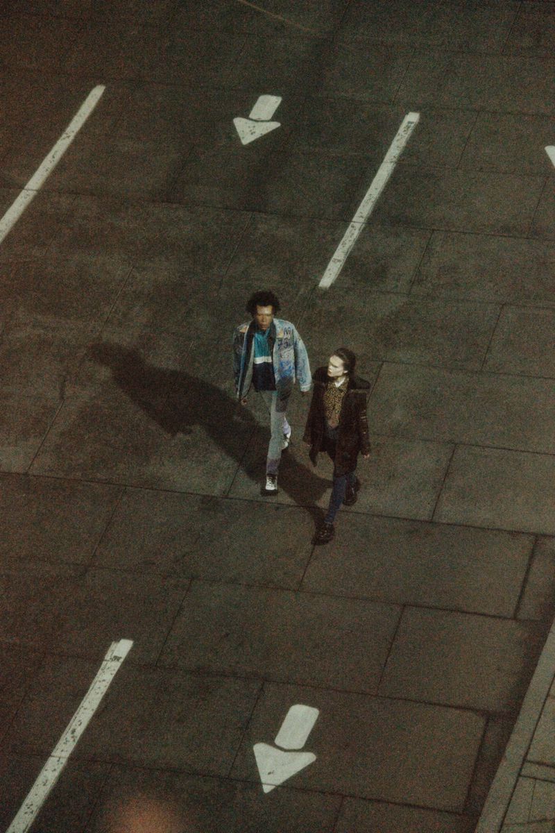 Overhead shot of two people walking on a city street with directional arrows painted on the pavement, captured in low lighting conditions.