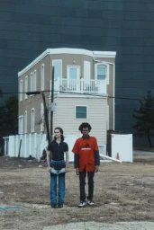 Two models standing outdoors in a desolate landscape before a small two-story building for the Snow Crash project.