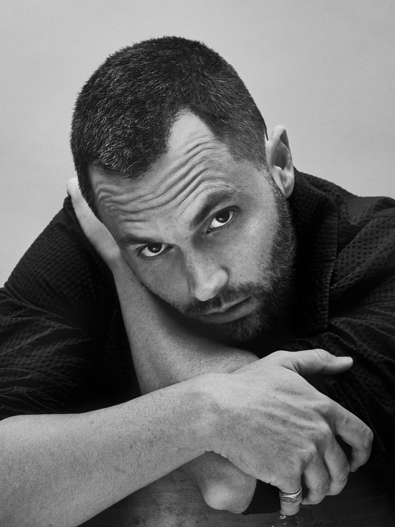Portrait of actor Penn Badgley resting his head on his crossed arms against a neutral grey background for Flaunt.