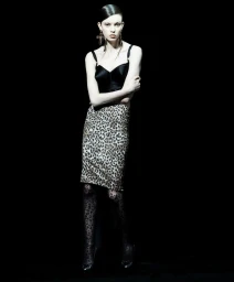 Model in black top and leopard print skirt wearing patterned tights against a dark background