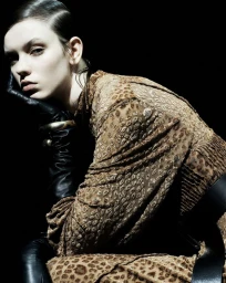 Model in animal print dress and black leather gloves posing against a black background for Vogue Adria