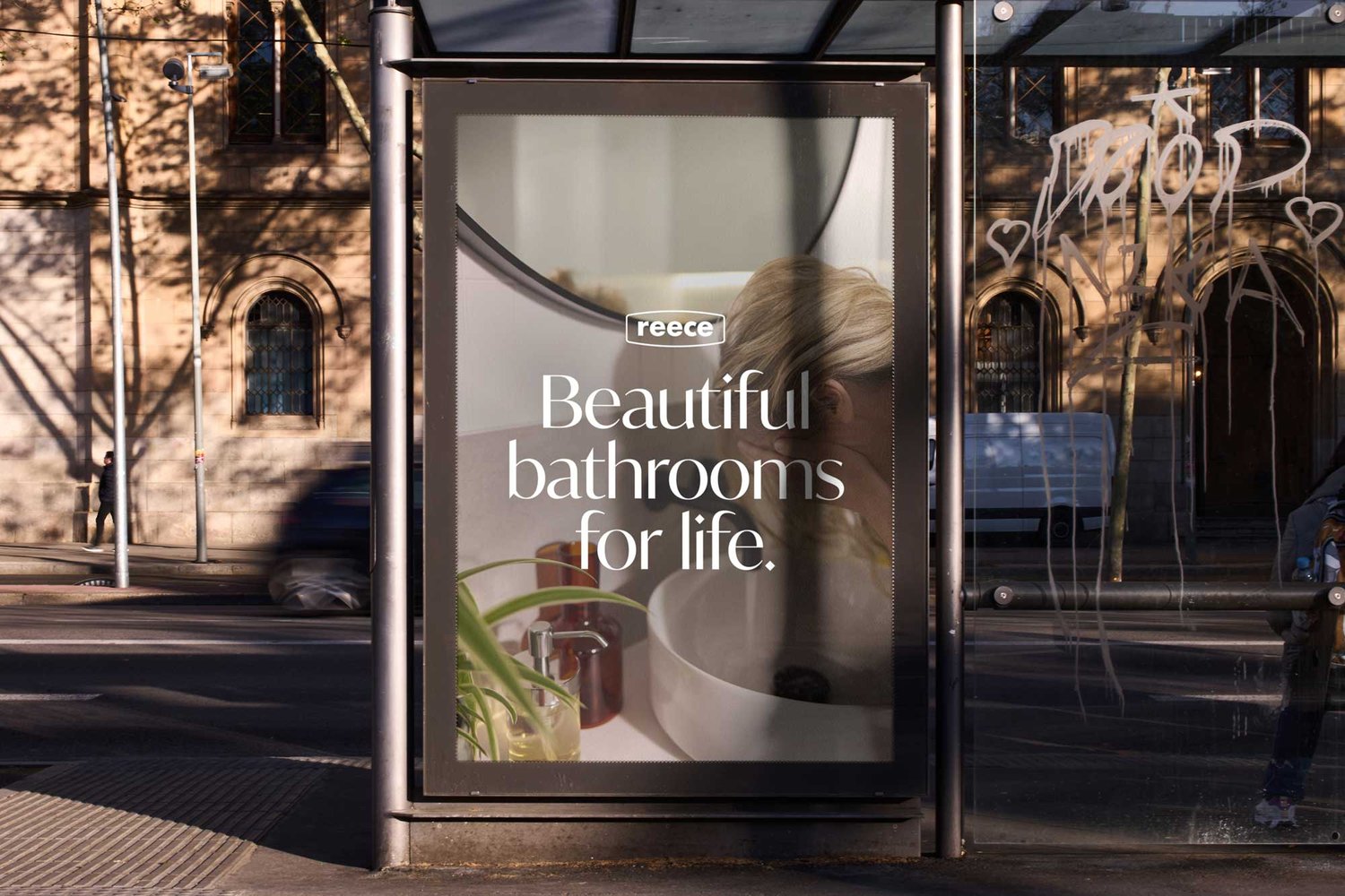 Outdoor bus stop advertisement featuring a modern bathroom design by Reece, displaying a vanity with accessories, shot in natural light.