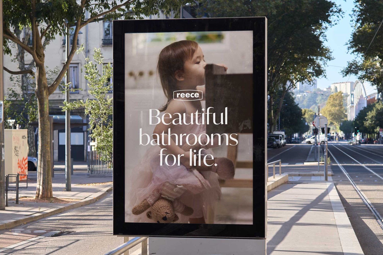 Outdoor advertising display featuring a young child holding a teddy bear for a 'Reece Beautiful bathrooms for life' advertisement.