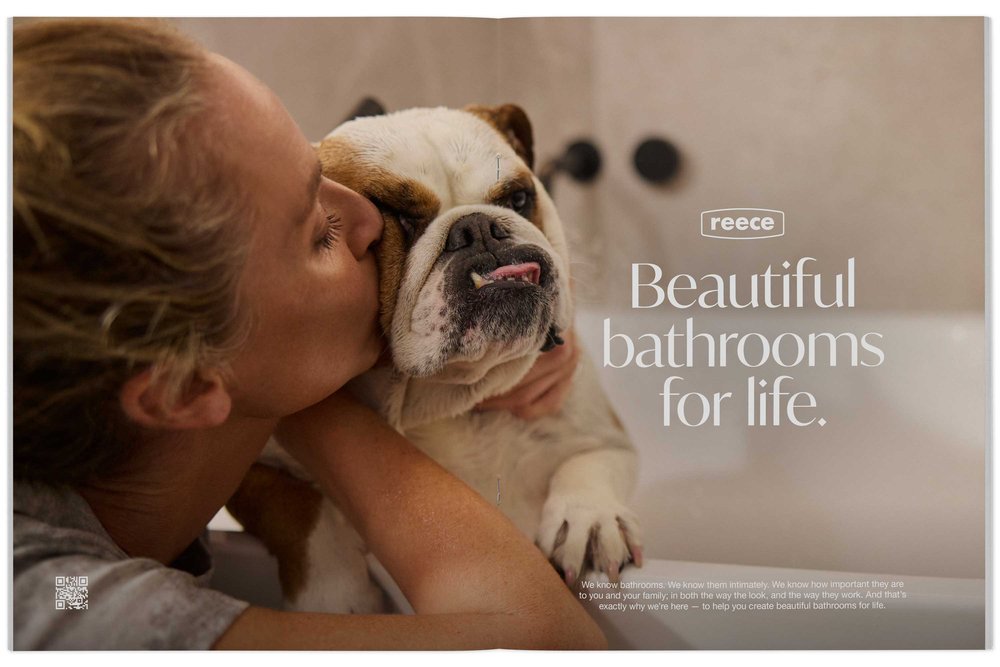 An adult female embraces a bulldog indoors, showcasing an advertisement for Reece bathrooms, promoting beauty and family.