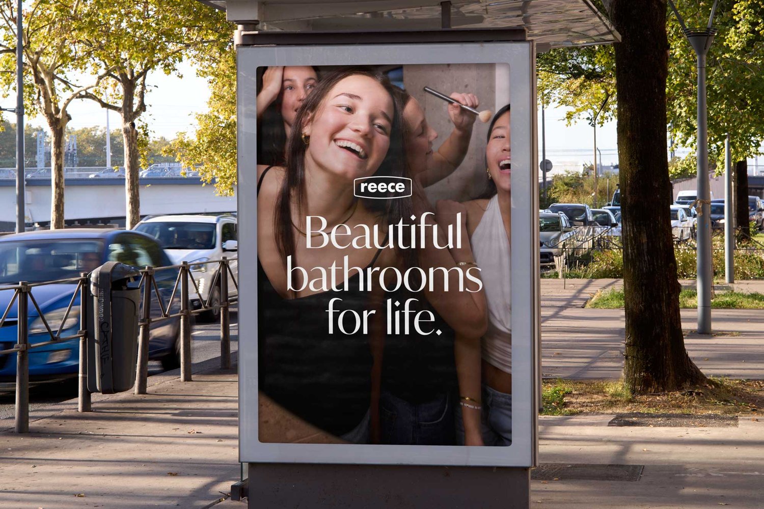 Outdoor advertisement featuring smiling women with cosmetic brushes for the brand Reece, seen on a city street during daylight.