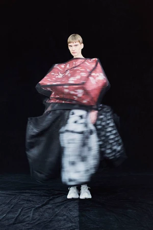 Model wearing voluminous sculptural avant-garde fashion with blurred motion against a black background