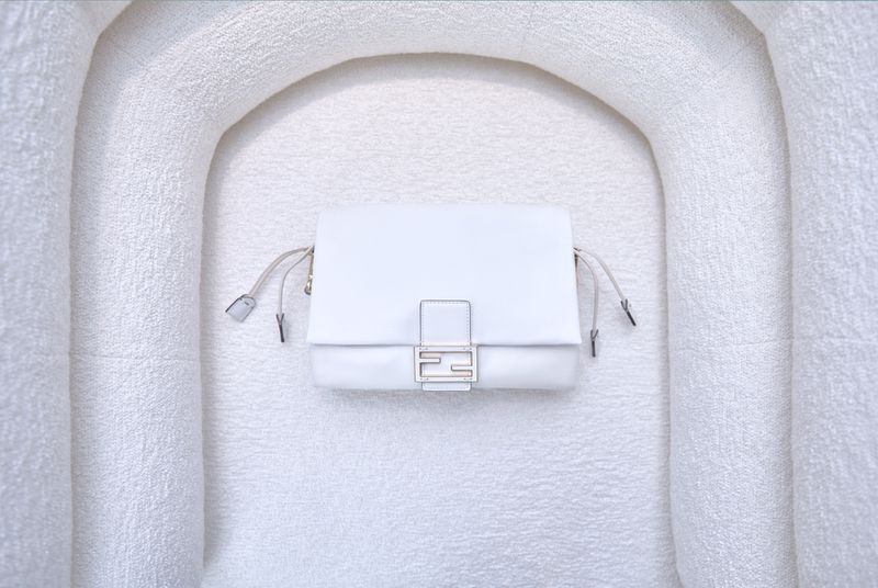 White Fendi First shoulder bag on a matching textured off-white surface in a minimalist product shot. Fashion product photography.