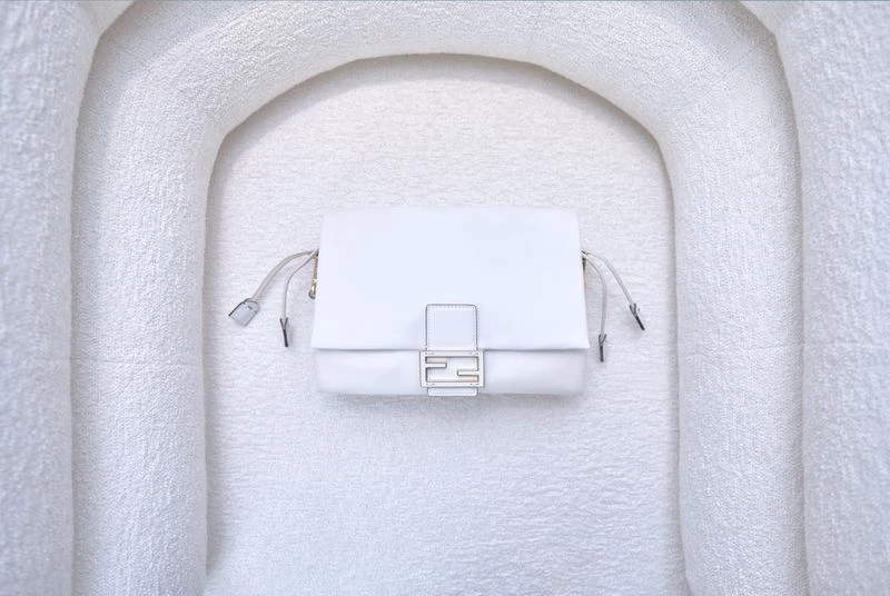 White Fendi First shoulder bag on a matching textured off-white surface in a minimalist product shot. Fashion product photography.