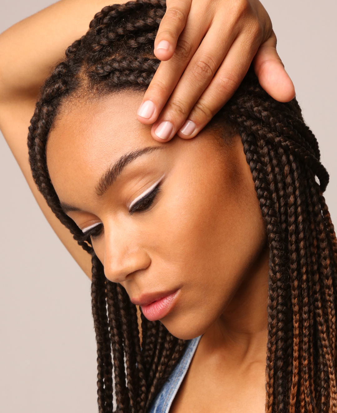 Close-up of an adult female with braided hair and white eyeliner in a studio setting with a neutral background.
