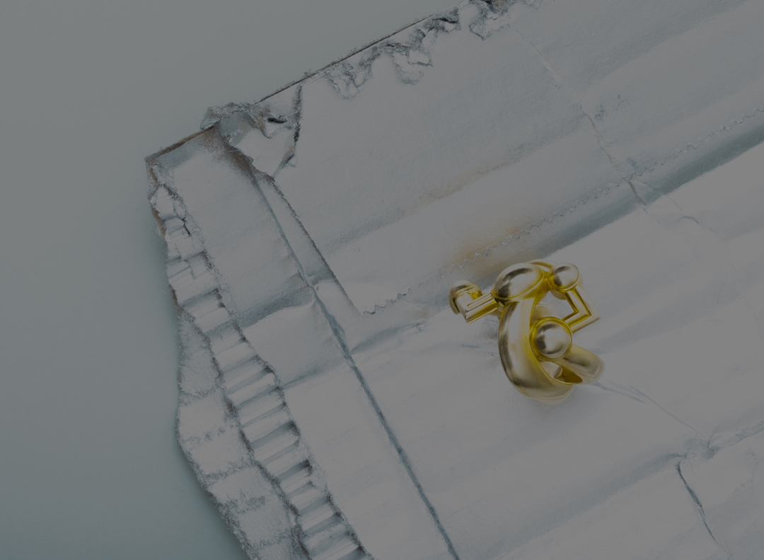 Close-up shot of a gold metal clasp hardware ring set against a textured, silver background with an industrial, modern aesthetic.