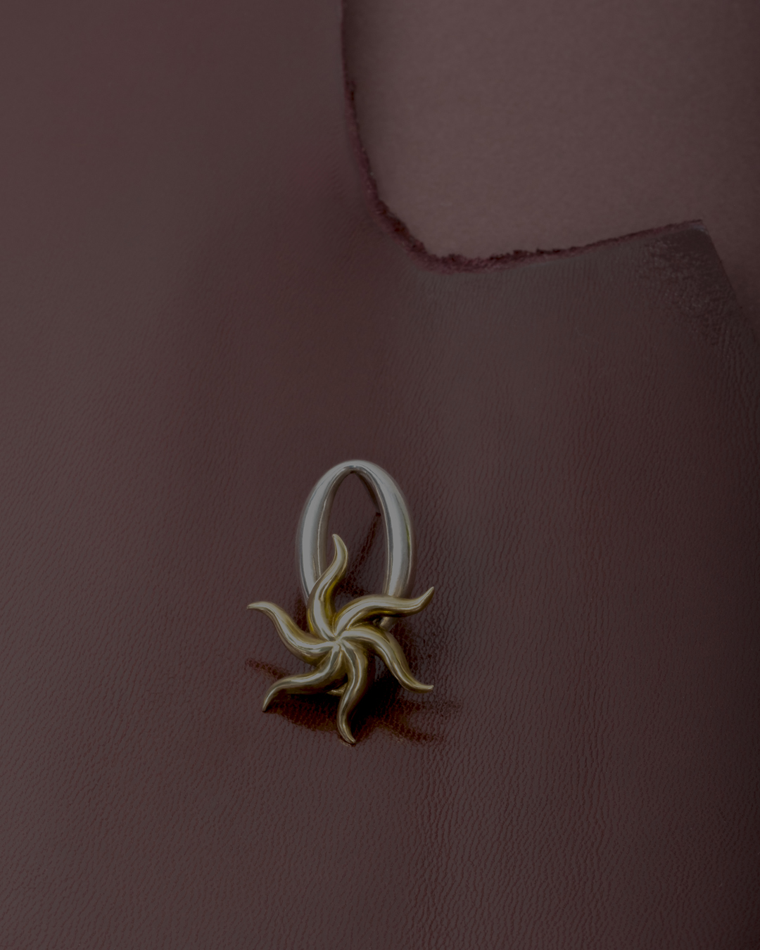 Close-up of a sculptural pendant with a silver loop and gold starburst design on a textured, deep brown surface.