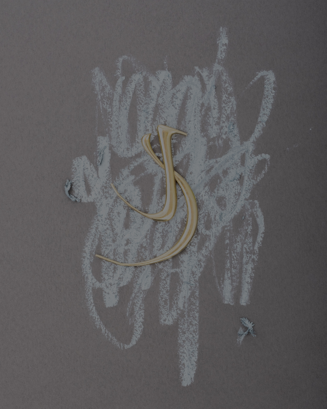 Abstract shot of a gold colored calligraphic 'S' shape over a background of white chalk scribbles on a grey-brown textured surface.