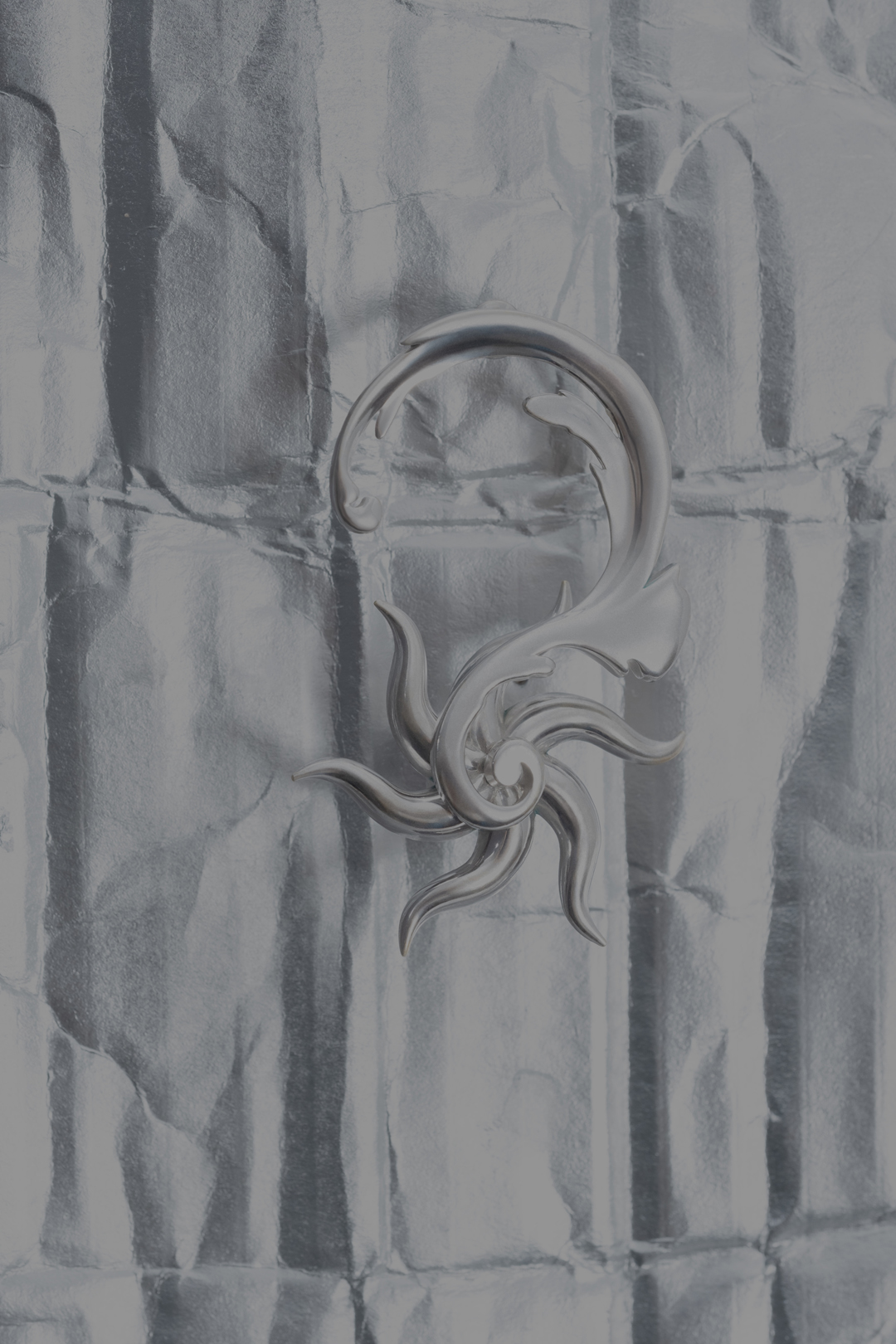 Silver artistic earring on a shiny wrinkled metal background. Fine art photography of jewelry design.