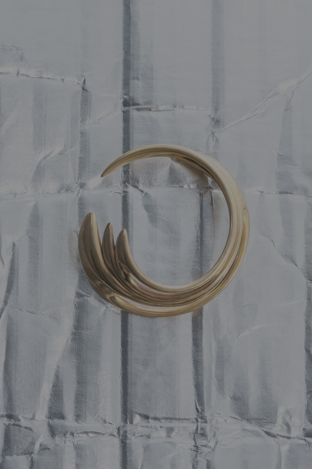 Abstract shot of a metallic gold, curved sculpture on a textured gray background with vertical lines and subtle, shiny reflections.