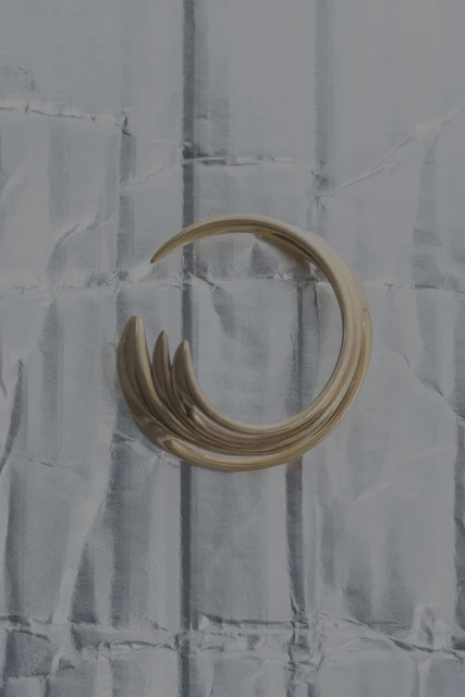 Abstract shot of a metallic gold, curved sculpture on a textured gray background with vertical lines and subtle, shiny reflections.