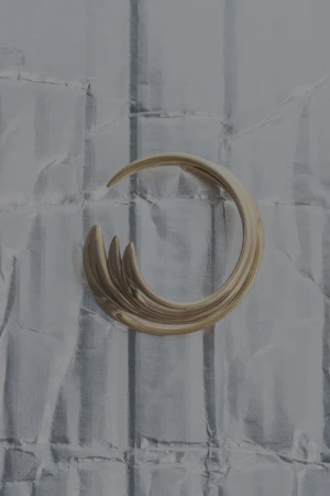 Abstract shot of a metallic gold, curved sculpture on a textured gray background with vertical lines and subtle, shiny reflections.