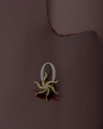 Close-up of a sculptural silver and gold ring against a deep burgundy leather background.