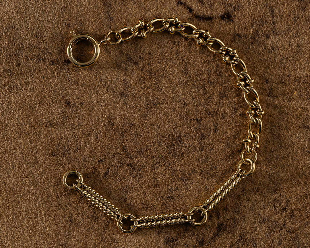 Close-up studio shot of a gold chain bracelet on a textured brown background, showcasing jewelry and precious metal details.