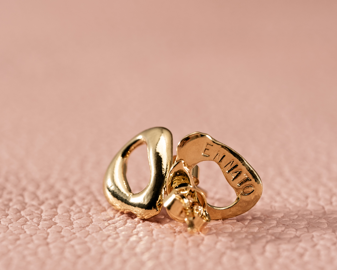 Close-up of gold hoop earrings on a pink leather surface, showcasing the jewelry's design and texture in a simple studio setting.