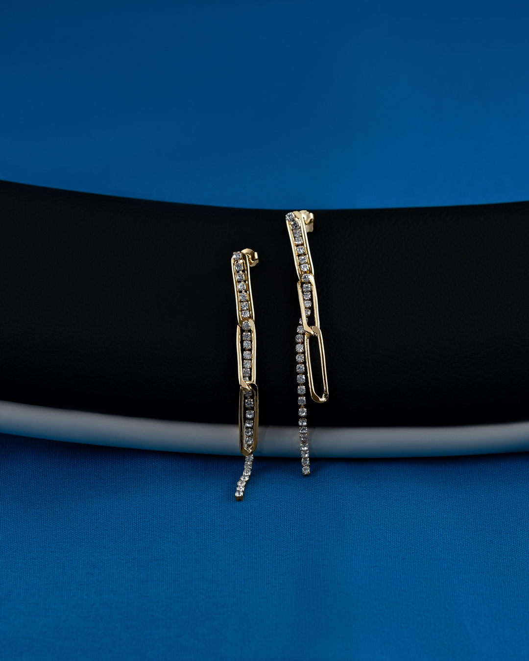 Pair of gold drop earrings with inlaid diamonds displayed on a black and blue surface in a studio product shot. Jewellery product photography.