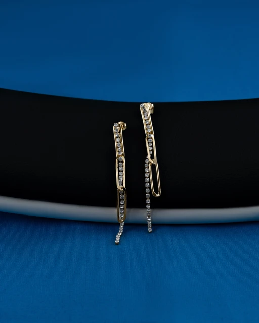 Pair of gold drop earrings with inlaid diamonds displayed on a black and blue surface in a studio product shot. Jewellery product photography.