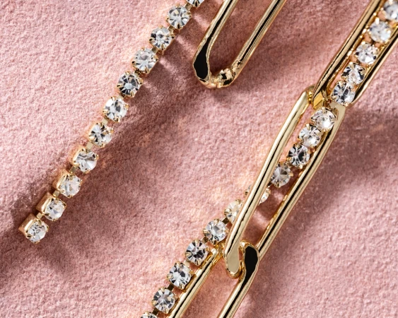 Close-up studio shot of gold-tone metal hair clips with inset rhinestones on a blush pink velvet surface. Shiny, luxurious accessories.