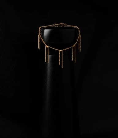 Gold tassel chain necklace displayed on a glossy black cylindrical pedestal against a dark black background.
