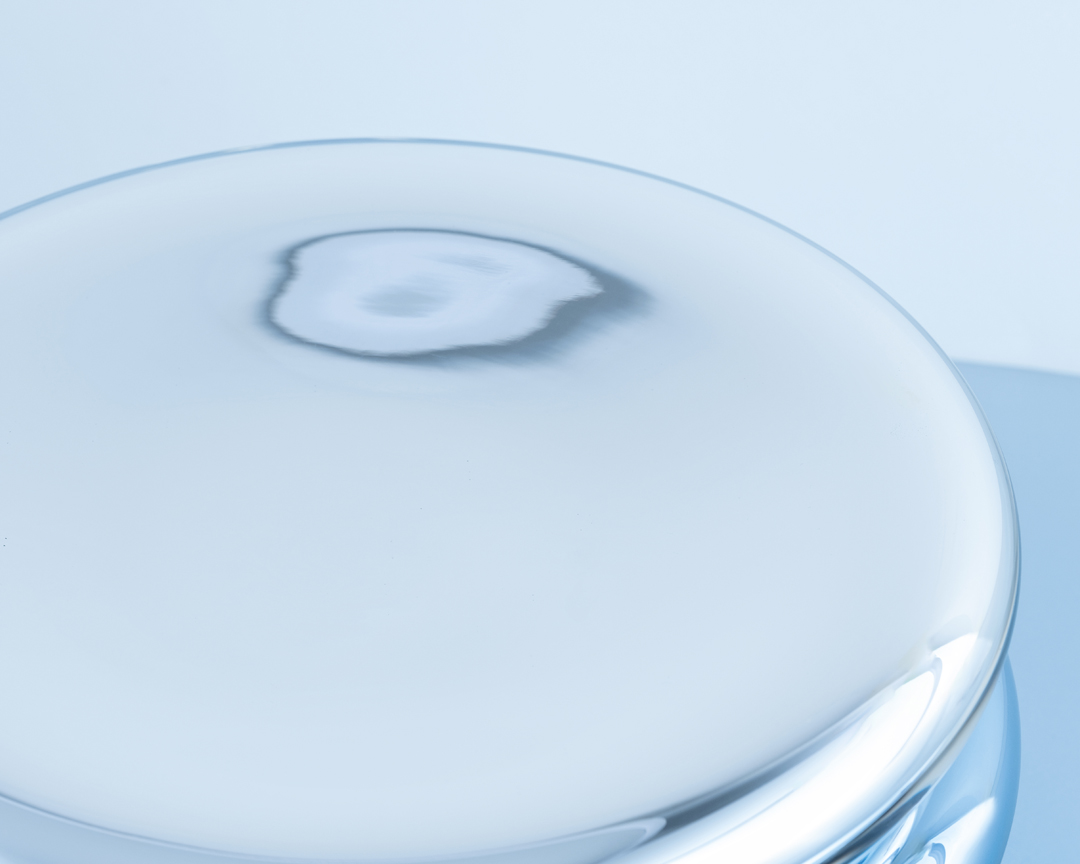 Abstract studio shot of a clear, rounded glass platform with a reflective surface, set against a soft, gradient blue background.