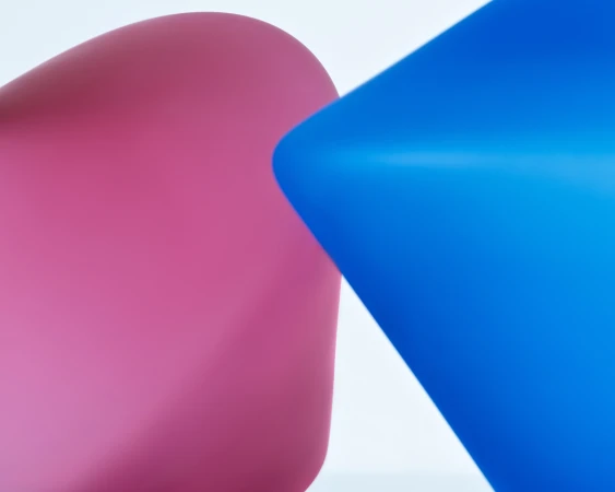 Close-up abstract still life showing a curved pink glass form alongside a sharp blue glass angle against a plain white background.