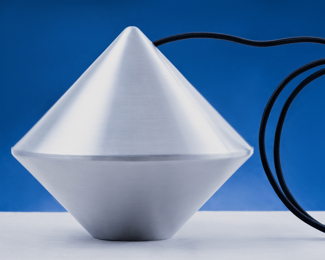 An abstract, gray geometric object is centrally placed against a blue gradient background with a black cord extending to the right.